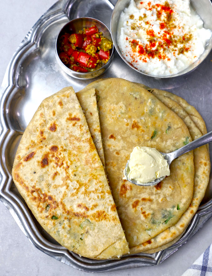 aerial shot of gobi paratha in a platter with a spoonful of butter and a bowl of masala curd
