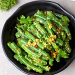 side close up shot of green beans salad in a black bowl.