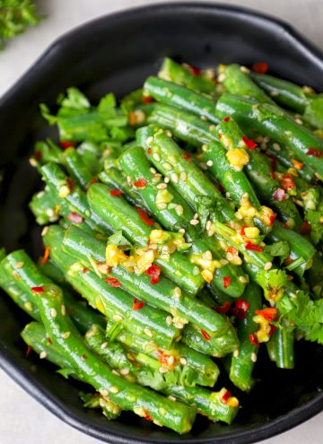 side close up shot of green beans salad in a black bowl.