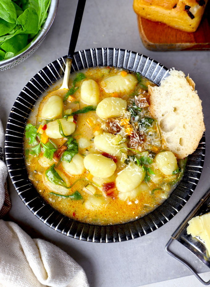 aerial shot of gnocchi soup served with bread in a black bowl.