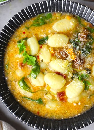 aerial close up shot of gnocchi soup in a black ceramic bowl.
