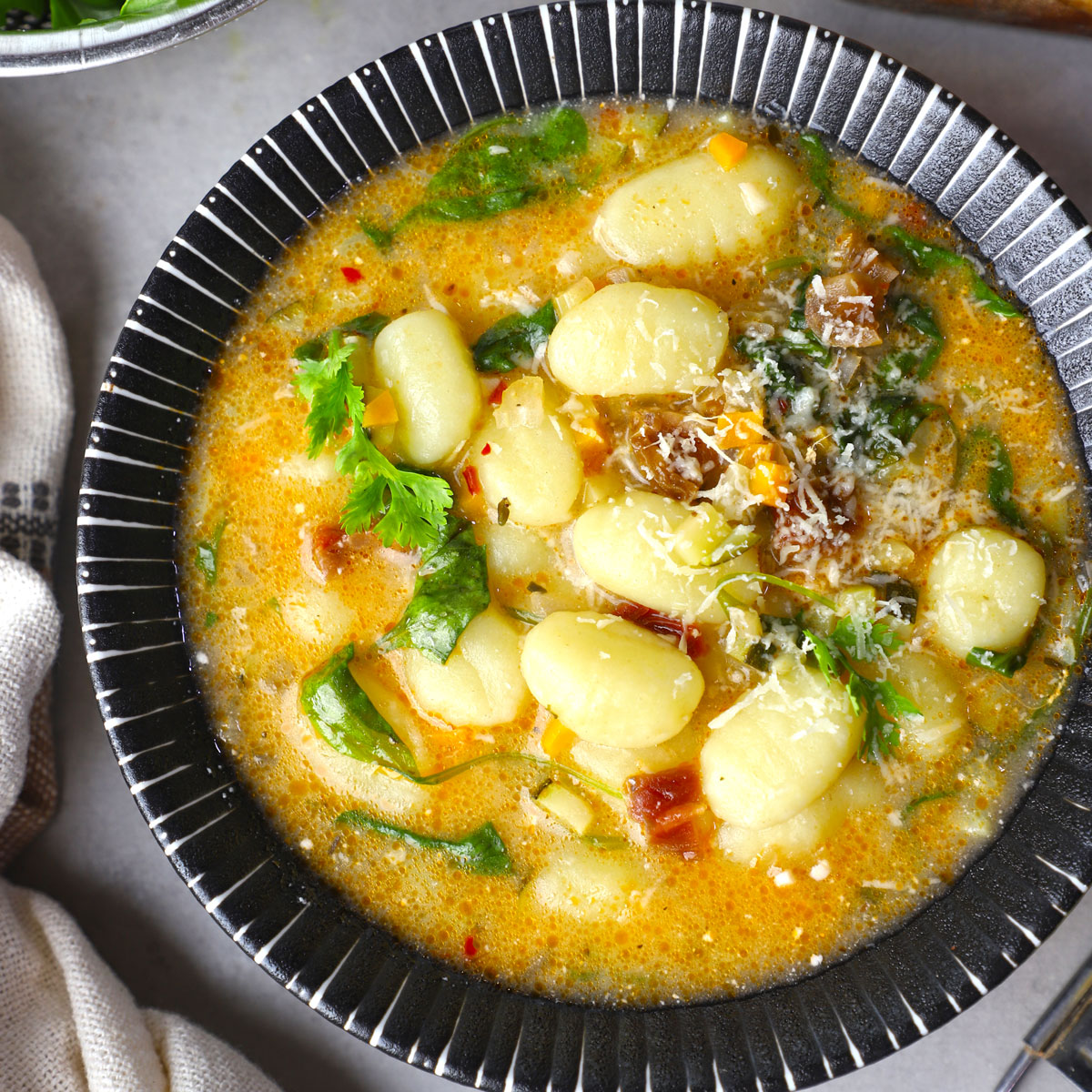 aerial close up shot of gnocchi soup in a black ceramic bowl.