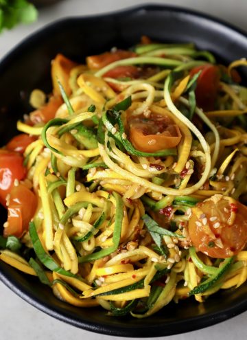side close up shot of zucchini noodles in a black bowl.