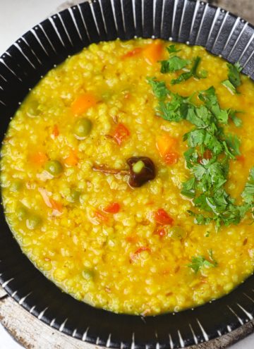 aerial shot of barley khichdi in a black serving bowl.