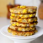 side close up shot of corn fritters stacked on a white plate.