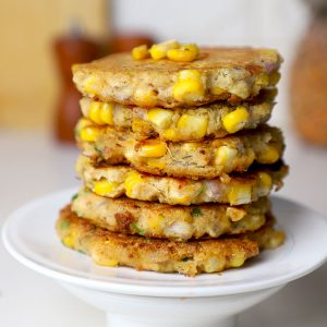 side close up shot of corn fritters stacked on a white plate.