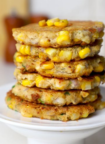 side close up shot of corn fritters stacked on a white plate.