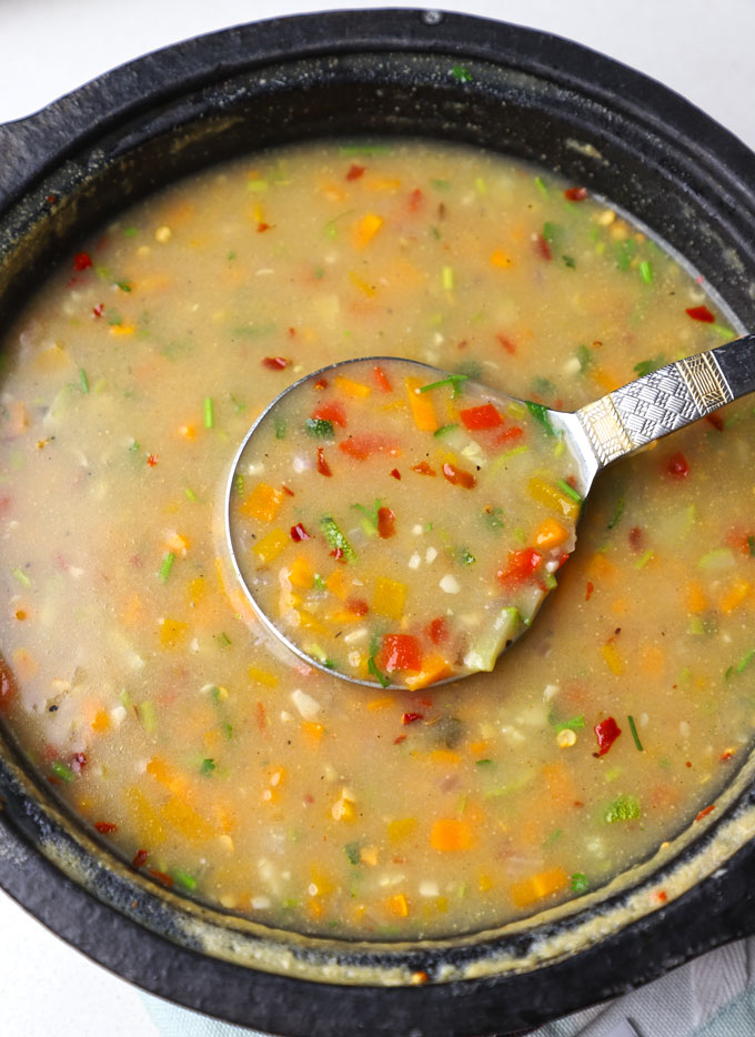 aerial shot of low calorie jowar soup served in a black stone pot with a ladle.